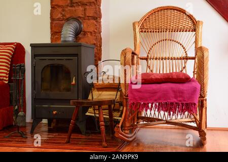Coin repos avec wicker chair en plus d'un poêle à bois, petit tas de bois de chauffage et certains accessoires cuisinière Banque D'Images