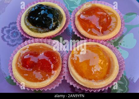 Pâte de barquettes rempli avec divers fruits confits, servi dans la plaque de verre rose sur bleu, voir Banque D'Images