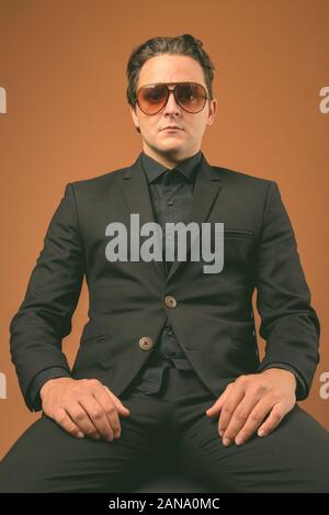 Studio shot of Italian businessman wearing costume noir contre fond brun Banque D'Images