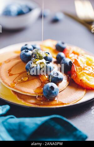 Verser le miel sur les crêpes avec des pêches et bleuets frais. Banque D'Images