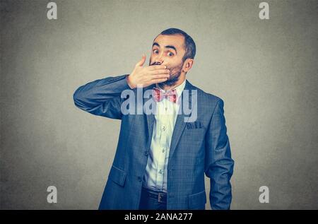 Jeune homme effrayé couvrant la bouche avec une main. Choqué l'émotion humaine face à l'expression. Course mixte modèle barbu isolé sur fond gris mur studio Banque D'Images