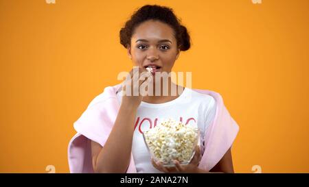 Bénéficiant d'adolescente de séries comiques à la tv eating popcorn sur fond orange Banque D'Images