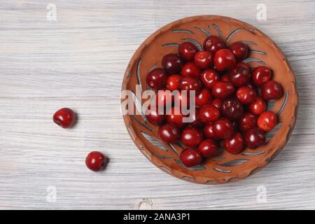 Cerises rouges d'argile dans un plat sur une table en bois blanc Banque D'Images