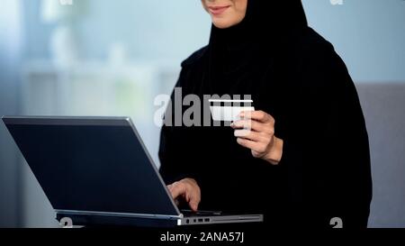 Jolie femme en hijab entrer le numéro de carte de crédit sur un ordinateur portable, les achats en ligne Banque D'Images