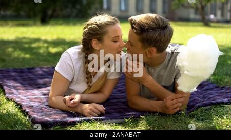 Les adolescents de manger de la barbe et essayant d'embrasser, allongé sur sac en park, les relations Banque D'Images