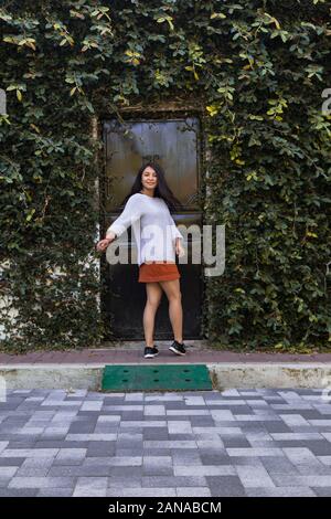 Jeune femme debout dans le quartier rue avec un mur de feuilles vertes Banque D'Images