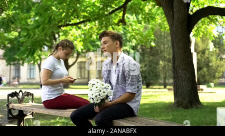 Teen timide de fleurs assis à côté de dame, le surf sur le net, l'hésitation de téléphone Banque D'Images