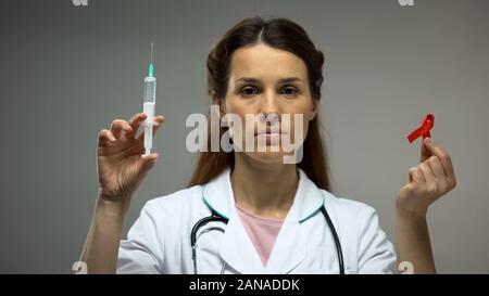 Femme médecin montrant ruban rouge et campagne de prévention du sida seringue, médicament Banque D'Images