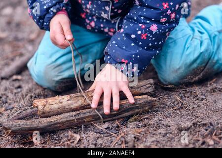 Libre de faible section d'un caucasien enfant fille vêtements chauds d'hiver de genou sur le sol forestier et jouant avec un morceau de bois et une chaîne d'un Banque D'Images