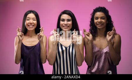 Smiling female friends crossing fingers, priant pour la bonne chance, rêves Banque D'Images