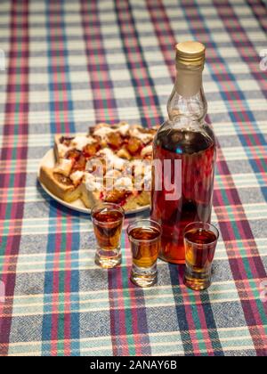 Bouteille de liqueur faite maison doogwood avec trois verres de vodka et la plaque de gâteau fait maison servi sur table Banque D'Images