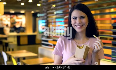 Jolie femme holding frites smiling, restauration rapide snack, client satisfait Banque D'Images