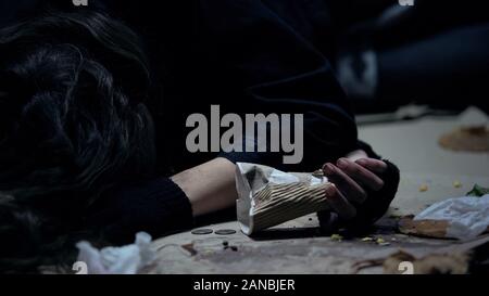 Sans-abri d'ébriété woman holding paper cup lying on floor dans un abri sale Banque D'Images