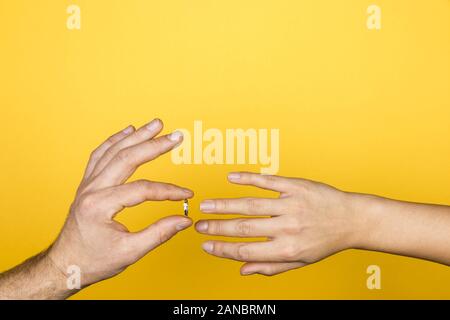 Close up of man main mettre une bague de fiançailles sur la main d'une femme sur fond jaune Banque D'Images