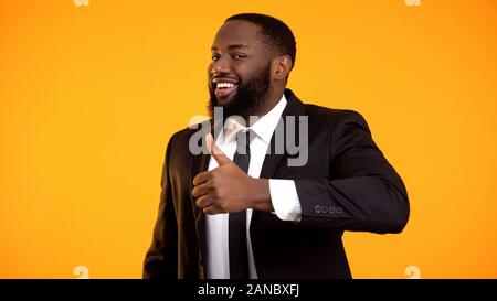 Smiling black man en habit d'affaires en litige faisant thumbs-up et à la recherche à la cam Banque D'Images