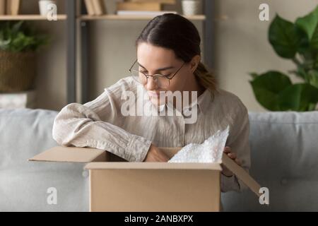 Heureux femme millénaire unboxing colis dans la salle de séjour. Banque D'Images