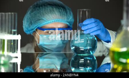 Female scientist holding uniforme de protection dans la fiole avec un liquide bleu, de l'analyse Banque D'Images