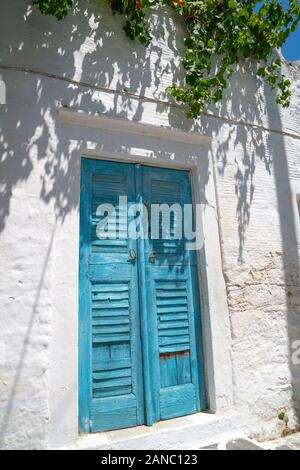 Scène de village typique de l'île grecque de Filoti à volets bleu porte dans mur blanc avec des branches surplombant Banque D'Images