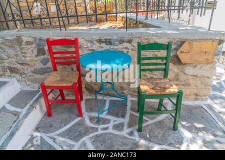 Two empty chairs on village path with blue table and blank wooden signboard in Greek Island village scene in Filoti. Banque D'Images