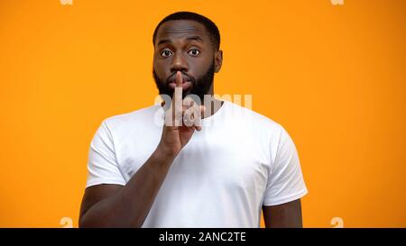 L'homme afro-américain montrant silence geste, gardant secret, fond jaune Banque D'Images