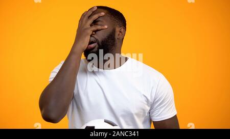 L'homme afro-américain avec ballon de soccer regarder match, montrant face signe palm Banque D'Images