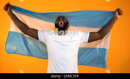 L'homme afro-américain de l'équipe sports réjouissance la victoire, tenant un drapeau de l'Argentine Banque D'Images