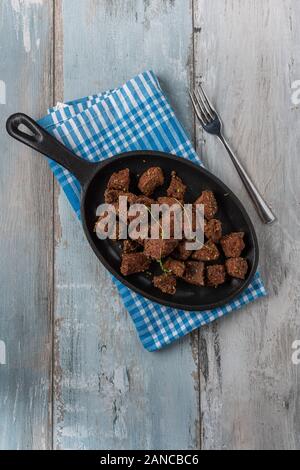 Cubes de foie frit en plaque noire sur fond de bois Banque D'Images