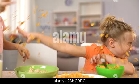 Happy little boy and girl throwing cornflakes les uns les autres, s'amusant à la maison Banque D'Images