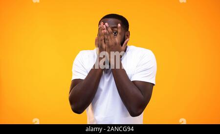 Surpris par african american guy peeping doigts sur fond jaune Banque D'Images