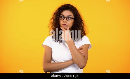 Jeune femme biracial lunettes en pensant à décision, fond jaune Banque D'Images