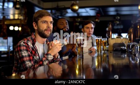 Anxieux pour acclamer amis multiraciale jeu de sport dans pub, regarder match à la télé Banque D'Images