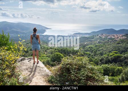 Young woman admiring panorama à partir de la colline qui surplombe le port de baie en Toscane denim dungaree Banque D'Images