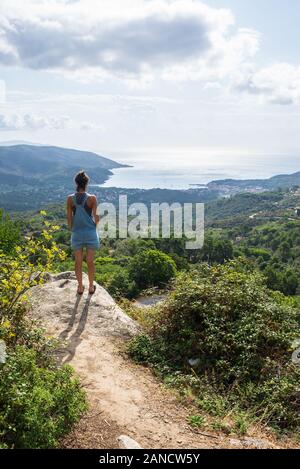 Young woman admiring panorama à partir de la colline qui surplombe le port de baie en Toscane denim dungaree Banque D'Images