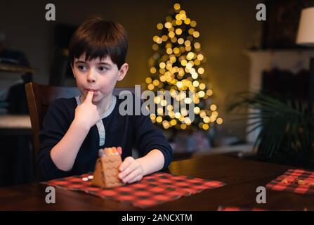 Jeune garçon décorant la maison de pain d'épice avec des bonbons à Noël. Banque D'Images