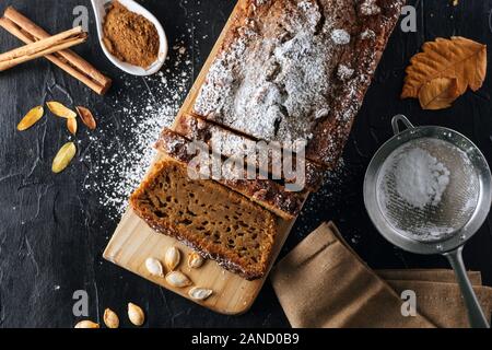 Passage télévision jeter vue d'un gâteau de potiron coupé en tranches avec du sucre en poudre sur le dessus, sur une planche de bois. La vie encore tourné d'une saison d'automne imag Banque D'Images