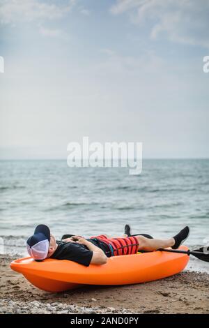 Homme prenant une sieste sur la plage en kayak pendant les vacances d'été Banque D'Images