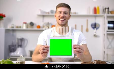 Cheerful man holding tablet avec l'écran vert, blogs de cuisine et de modèle d'applications Banque D'Images