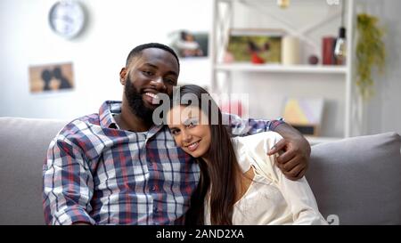 Heureux couple hugging multiethnique et à la caméra, à l'ensemble de détente Banque D'Images