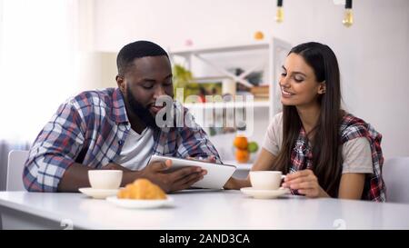 La famille de race mixte à défiler sur tablet pc pendant le petit-déjeuner, les achats en ligne Banque D'Images