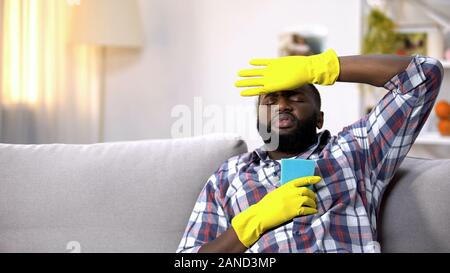 Fatigué de l'homme dans les gants assis sur un canapé, se détendre après le nettoyage de la maison Banque D'Images