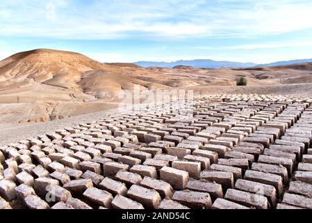 Le séchage des briques de boue dans le désert marocain avec ses dunes de sable et les contreforts de l'Atlas en arrière-plan. Le paysage est sous un ciel bleu Banque D'Images