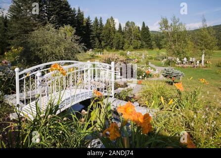 Frontière avec l'hémérocalle - Hemerocallis orange et fleurs en fer forgé blanc metal passerelle sur étang dans cour privée pays jardin en été. Banque D'Images