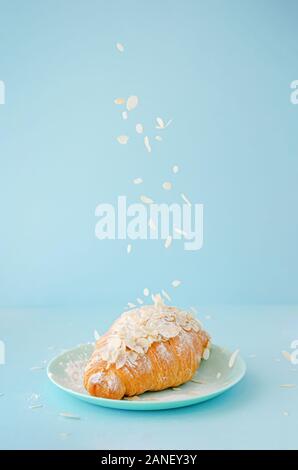 Flocons d'amandes de tomber sur des croissants adossés sur fond bleu. L'espace de copie, à la verticale. Banque D'Images