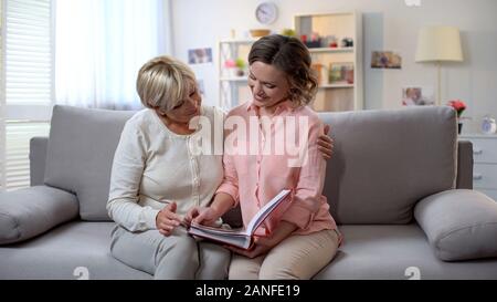 Senior lady avec sa fille adulte regarder des photos de l'album ensemble, souvenirs de famille Banque D'Images