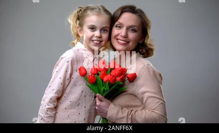 Mother and Daughter hugging and looking at camera, holding Flowers, mums jour Banque D'Images