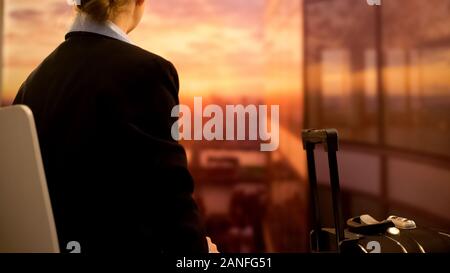 Femme avec valise assis à l'aéroport et profiter de magnifiques couchers de soleil, vue de dos Banque D'Images