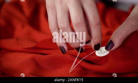 Close-up couture mains gros bouton rouge au tissu, matériel de décoration, d'inspiration Banque D'Images