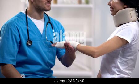 Traumatologist holding mesdames part dans elastic wrap, flirter avec la jolie patiente Banque D'Images