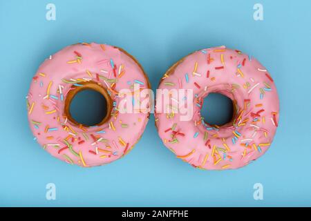 Sweet donuts rose sur fond bleu, présenté sous la forme d'yeux, vue d'en haut. Desserts, jeu des couleurs, fond bleu Banque D'Images