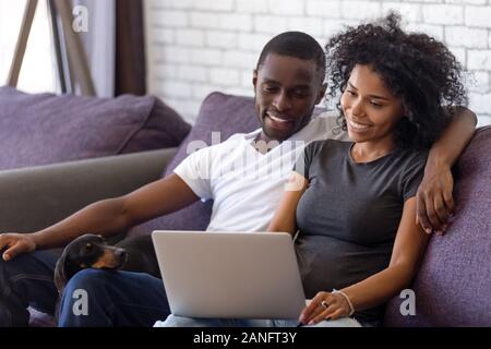 Happy black couple vous détendre avec chien regarder la vidéo sur l'ordinateur portable Banque D'Images